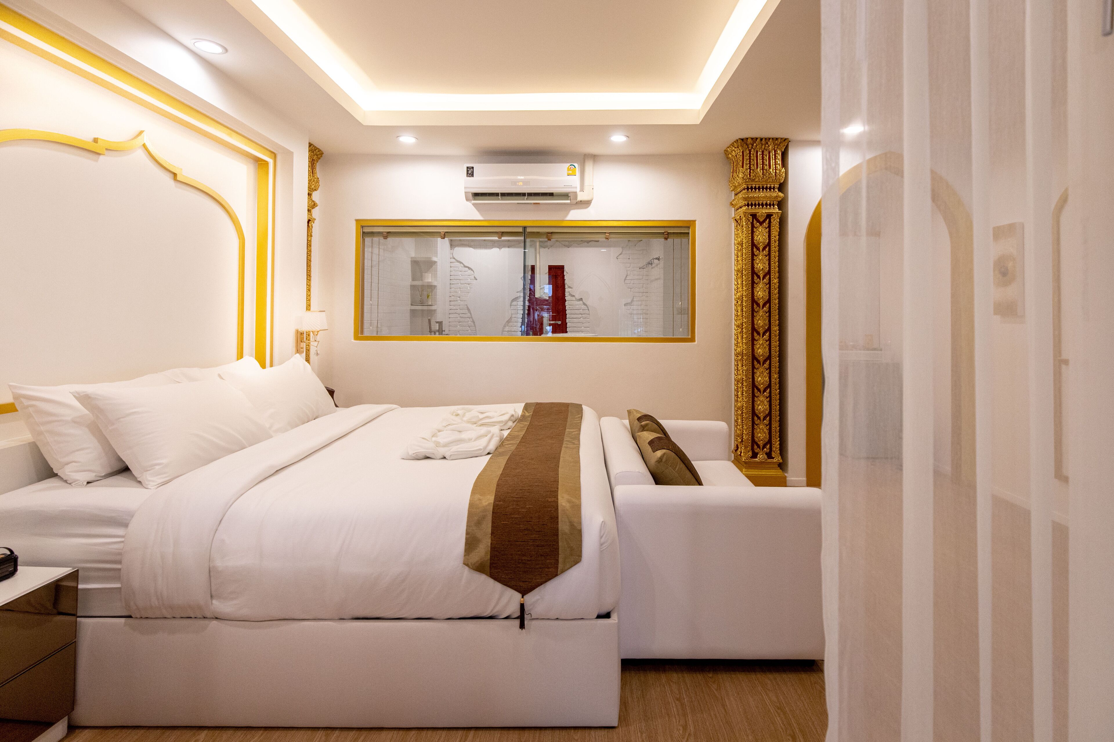 A modern hotel room with a large bed, a bedside table, a small sofa, and a window with a view of a building.