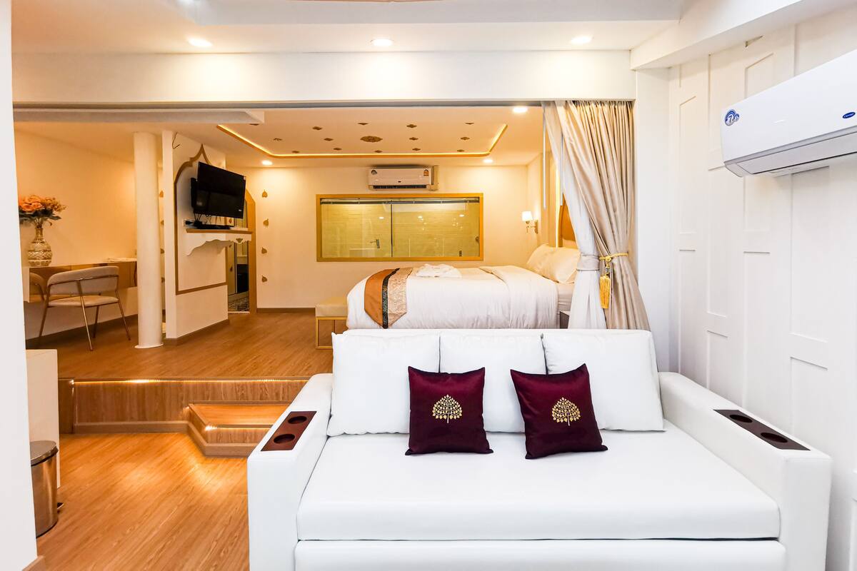Une chambre d’hôtel moderne, équipée d’un canapé, de deux coussins décoratifs, d’une télévision, d’un bureau avec une chaise et d’une grande fenêtre.