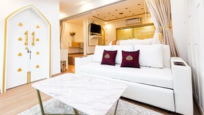 Una habitación de hotel moderna con un sofá blanco, una mesa de centro de mármol y un ventanal con cortinas.