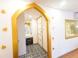 Un pasillo con piso blanco y negro estampado, una puerta blanca con detalles dorados y un espejo en la pared.