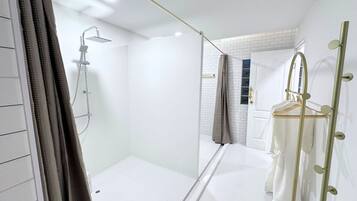 A modern bathroom with a glass shower enclosure, a white tiled floor, and a mirror with a gold frame.