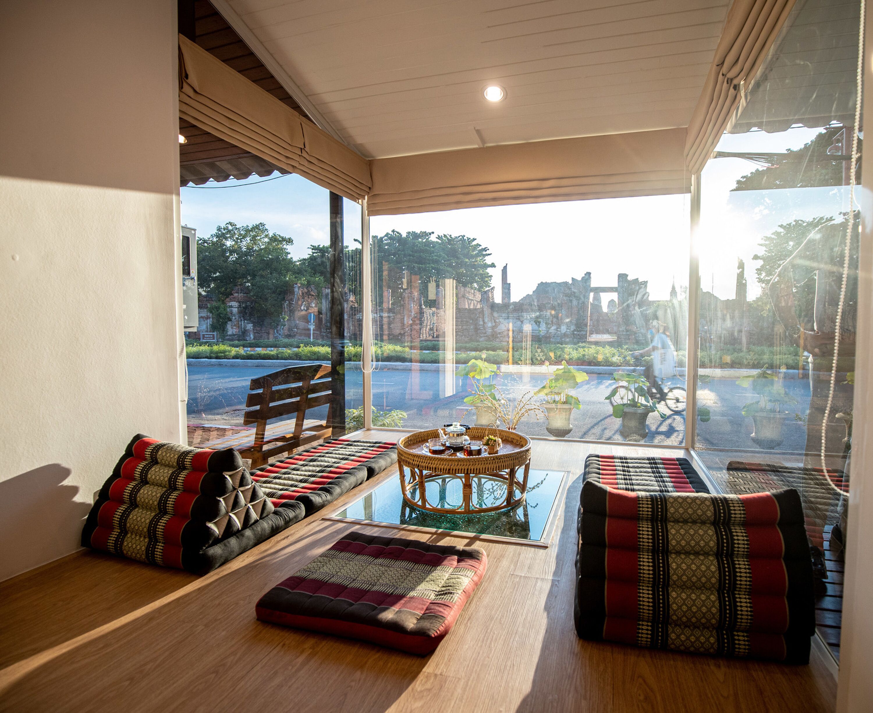A room with a wooden floor, a bench, a table with a basket, and a view of a street and greenery outside.