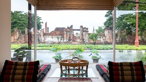 Una habitación con vistas a antiguas ruinas a través de amplios ventanales, una mesa de mimbre con una bandeja y cojines tradicionales.