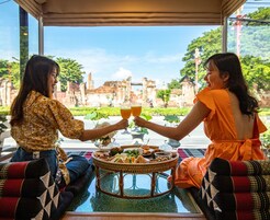 Dos personas brindando con bebidas en una mesa con vista a ruinas antiguas.
