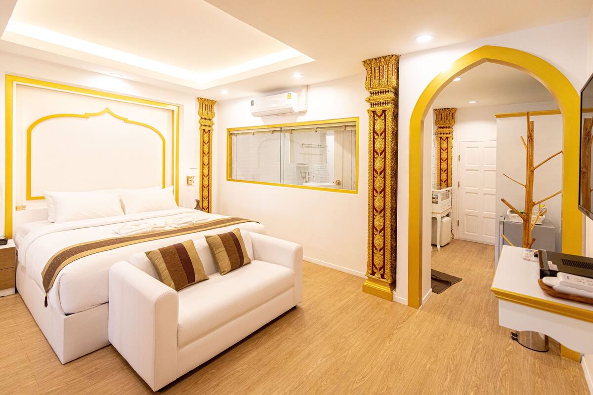Une chambre d’hôtel moderne, dotée d’un grand lit, d’un canapé, d’un bureau et d’une salle de bain visible à travers une arche.
