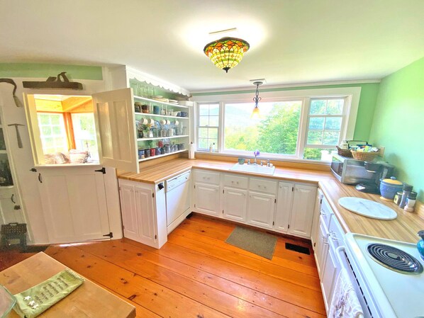 Een keuken met witte kastjes, een houten aanrecht, een spoelbak en een fornuis. Er is een raam met uitzicht op groen.