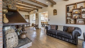 A cozy living room with a fireplace, wooden beams, a leather sofa, and a rustic brick wall.