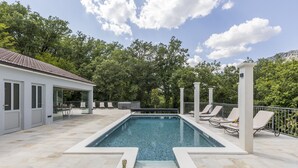 A swimming pool with a tiled deck, surrounded by lounge chairs and a covered patio area.