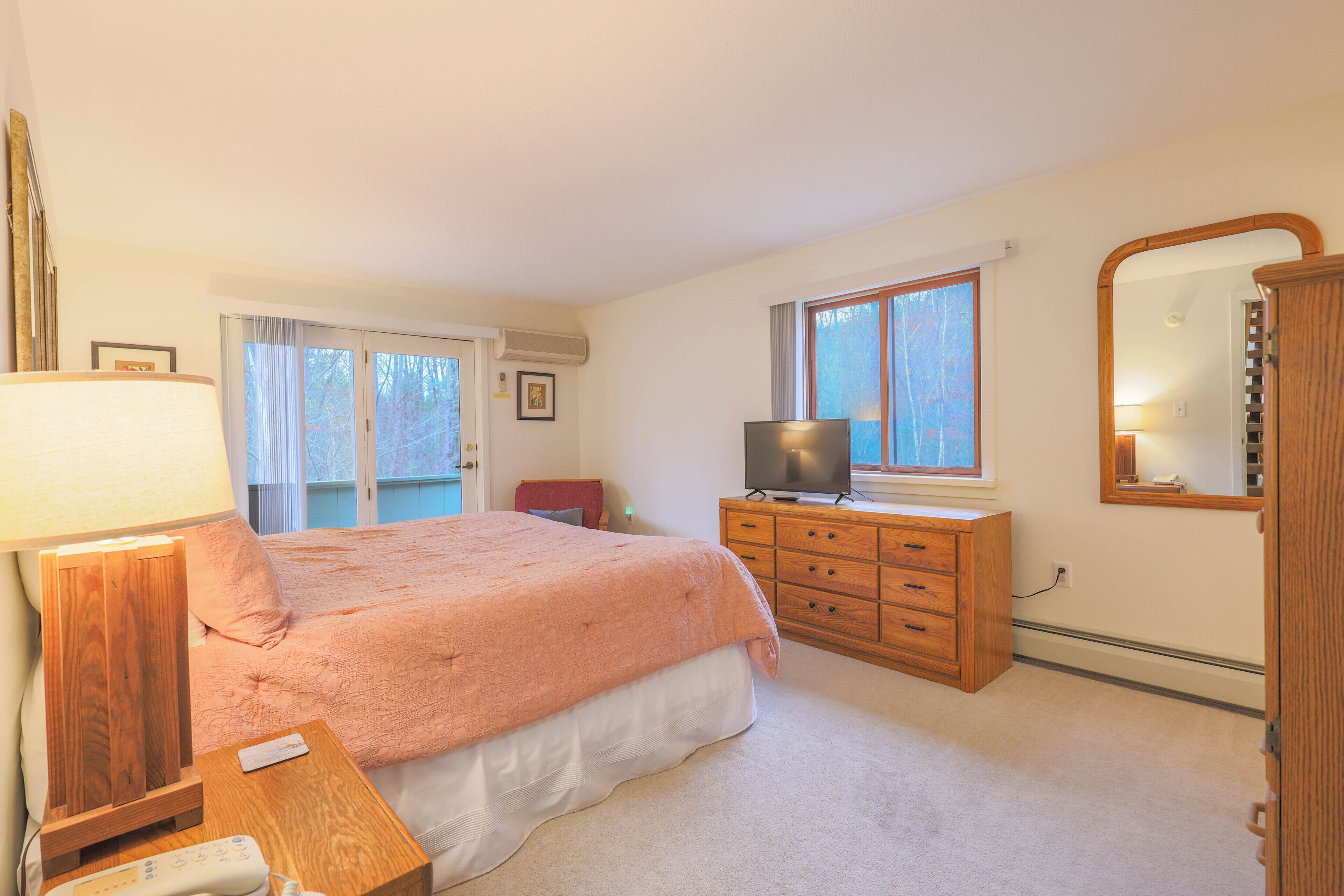 Een slaapkamer met een bed, een dressoir, een televisie, een lamp en een raam.
