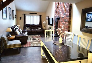 A living room with a sofa, armchairs, a dining table, and a brick wall.