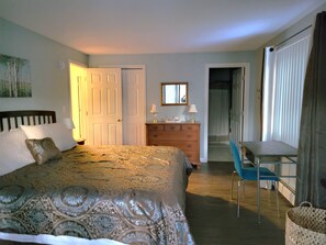 A bedroom with a bed, dresser, chair, and a door leading to a bathroom.