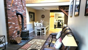 Una sala de estar acogedora con chimenea, un sofá de cuero, una mesa de comedor con sillas y una cocina al fondo.