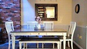 Un comedor con una mesa de madera, sillas blancas, un jarrón con flores y un espejo en la pared.
