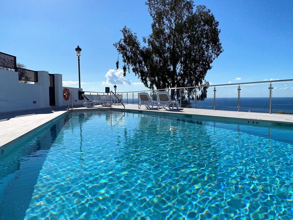 A clear blue pool with lounge chairs and a lifebuoy on the side, overlooking a scenic view.