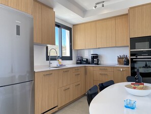 A modern kitchen with wooden cabinets, a stainless steel refrigerator, a coffee maker, and a dining table with chairs.