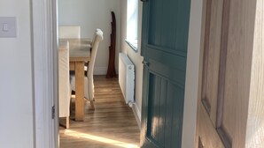 A hallway with a wooden floor, a dining area with a table and chairs, and a teal door.