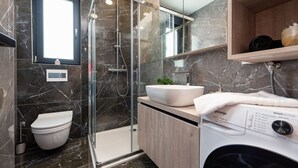 A modern bathroom with a glass-enclosed shower, a toilet, a sink, and a washing machine.