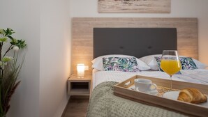 A neatly made bed with a pillow, a bedside table with a lamp, a tray with a croissant, a glass of orange juice, and a cup.