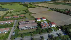 Oversigtsbillede af et boligområde med huse, en stor åben mark og et vandareal i baggrunden.