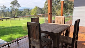 Une terrasse en bois avec une table et des chaises, donnant sur un champ verdoyant et des arbres.