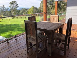Een houten terras met een tafel en stoelen, met uitzicht op een grasveld en bomen.