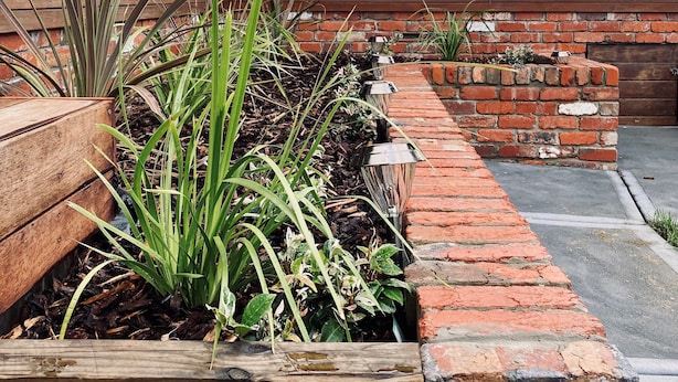 Un jardin sur le toit, agrémenté de jardinières en bois, de murs en briques et d’une rambarde en verre offrant une vue sur le paysage urbain.