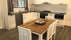 Une cuisine moderne avec des meubles blancs, une table à manger en bois et un mur de briques visible à travers la fenêtre.