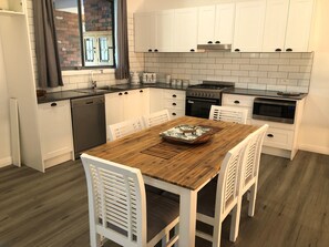 Een moderne keuken met witte kasten, een houten eettafel en een bakstenen muur die door het raam zichtbaar is.