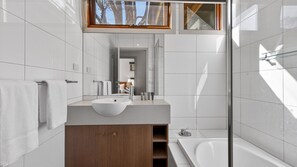 Ein modernes Badezimmer mit einem großen Spiegel, einem Waschbecken, einer Dusche und einem Holzkabinett.