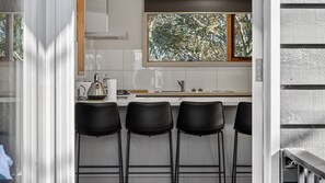 A modern kitchen with a large window, a kettle, and four black bar stools.