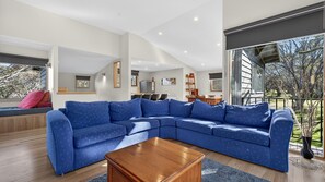 A modern living room with a large blue sectional sofa, a wooden coffee table, and a dining area with a kitchen in the background.