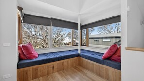 A room with a built-in bench along the window, a wooden floor, and a view of trees and a building outside.