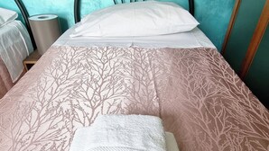 Een net opgemaakt bed met een witte handdoek en een deken met een boommotief. Het bed heeft een hoofdbord en staat tegen een blauwgroene muur.