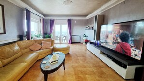 Een woonkamer met een leren bank, een salontafel, een flatscreen televisie en een balkon met plantenpotten.