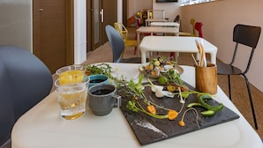 Ein Essbereich mit einem Tisch für zwei Personen, mit einer schwarzen Schiefertafel, auf der Salat, zwei Gläser mit einem klaren Getränk und eine Holzbecher zu sehen sind.