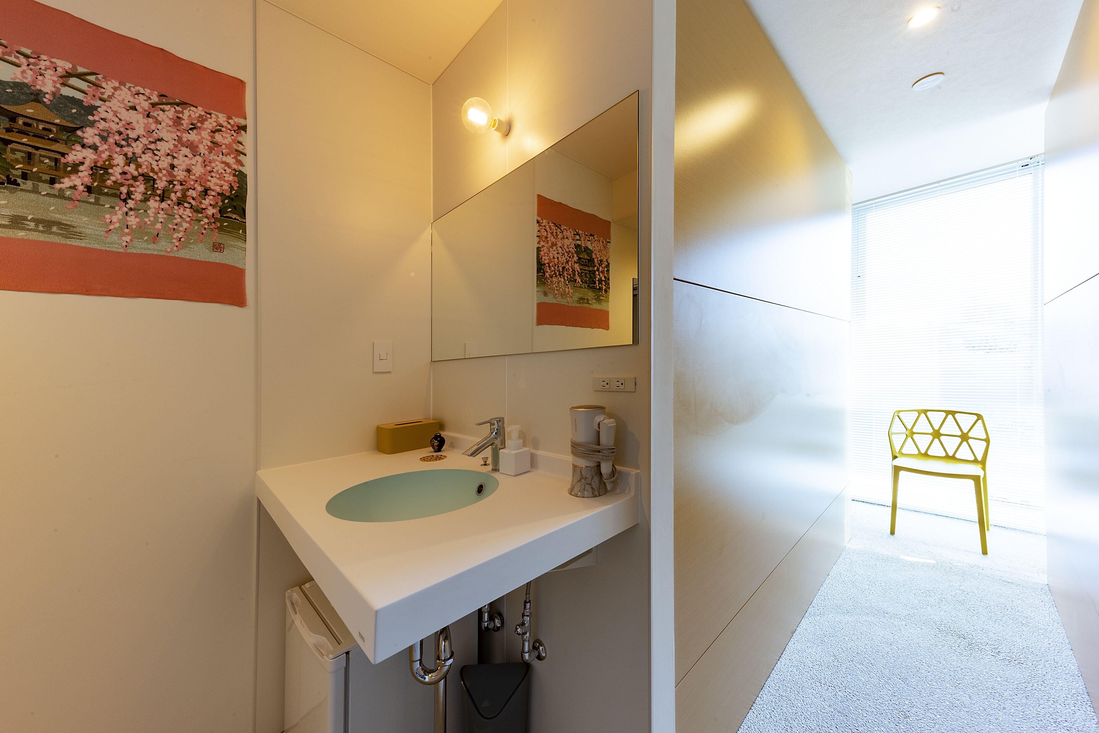 Un baño moderno con un lavamanos blanco, un espejo y una silla amarilla.