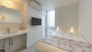 Ein Schlafzimmer mit einem Bett, einem großen Spiegel, einem an der Wand montierten Fernseher und einem Fenster mit Jalousien.
