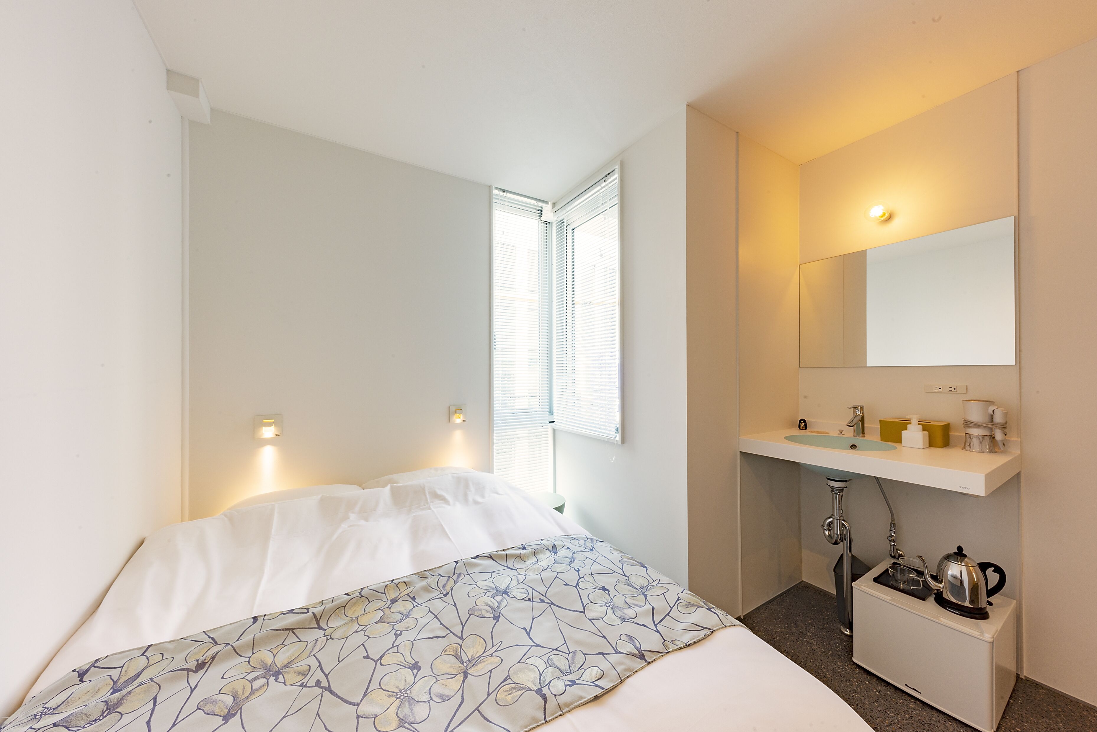 A hotel room with a bed, a small bathroom with a sink and mirror, and a window with blinds.