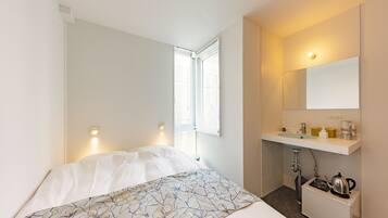 A hotel room with a bed, a small bathroom with a sink and mirror, and a window with blinds.
