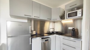 A compact kitchen with stainless steel appliances, including a refrigerator, oven, and microwave. - Cozy Air-Conditioned Apartment for 2 with Terrace, Near Beach, Fully Equipped Kitchen (Cap d'Agde naturisme)