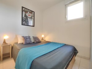 A bedroom with a bed, two bedside lamps, a window, and a poster on the wall.