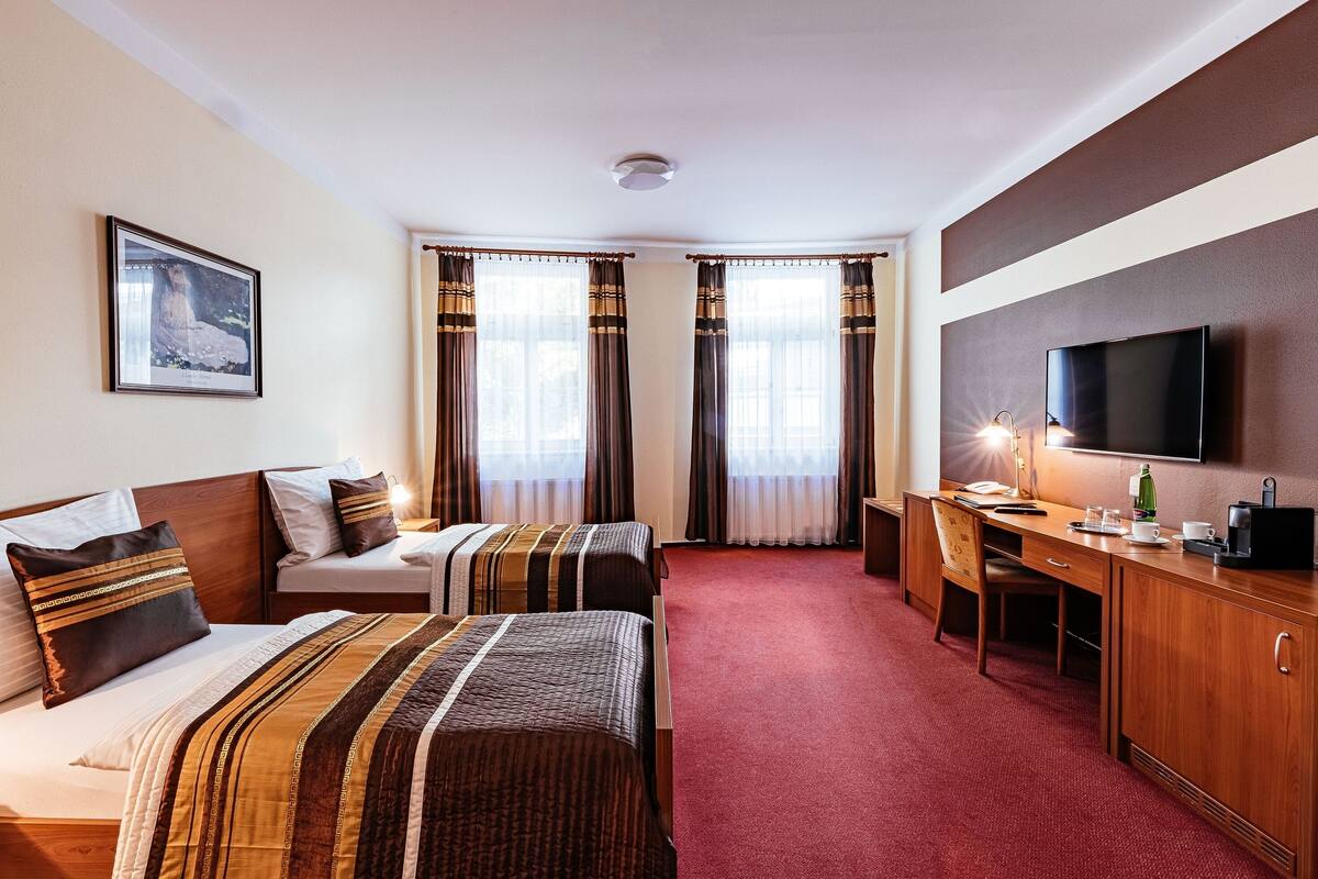 A hotel room with two beds, a desk, a chair, a television, and a framed picture on the wall.