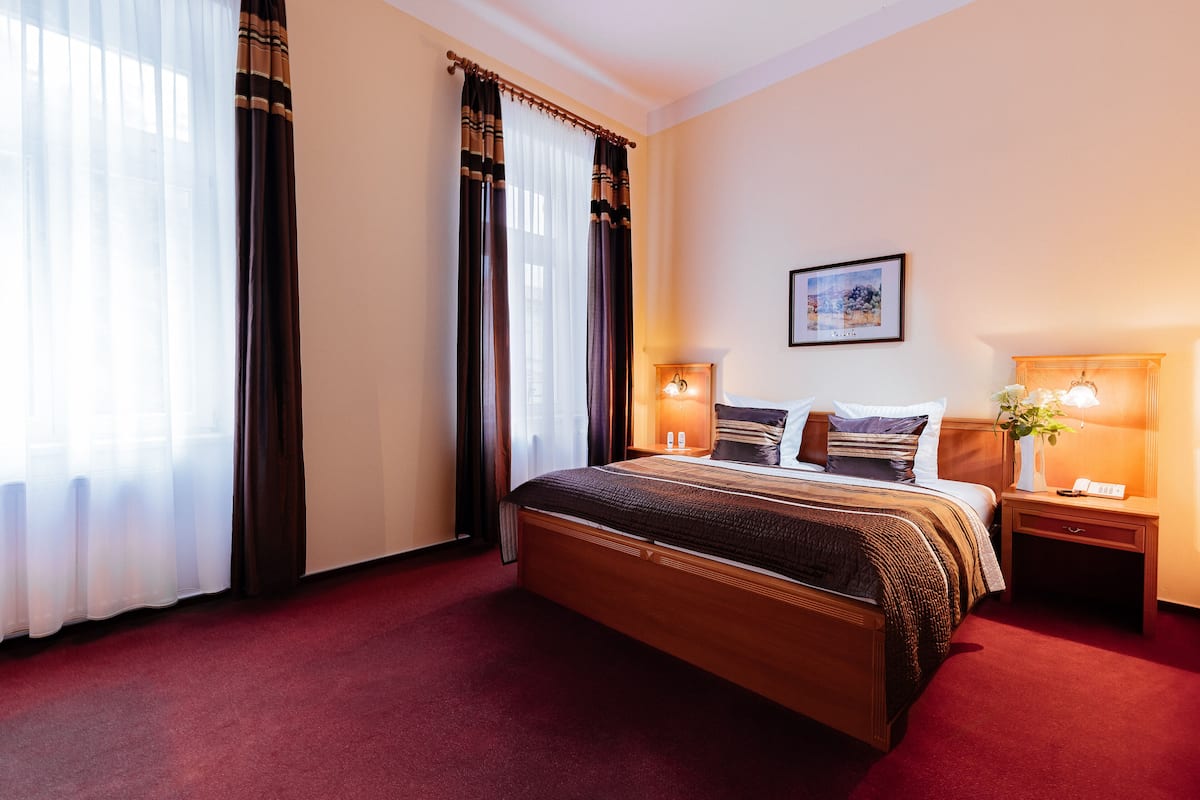 A hotel room with a large bed, two bedside tables with lamps, a framed picture on the wall, and a window with curtains.