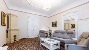 A room with a patterned carpet, a white coffee table with books, a grey sofa, and a white fireplace. - Reitenberger Spa Medical (Marianske Lazne)