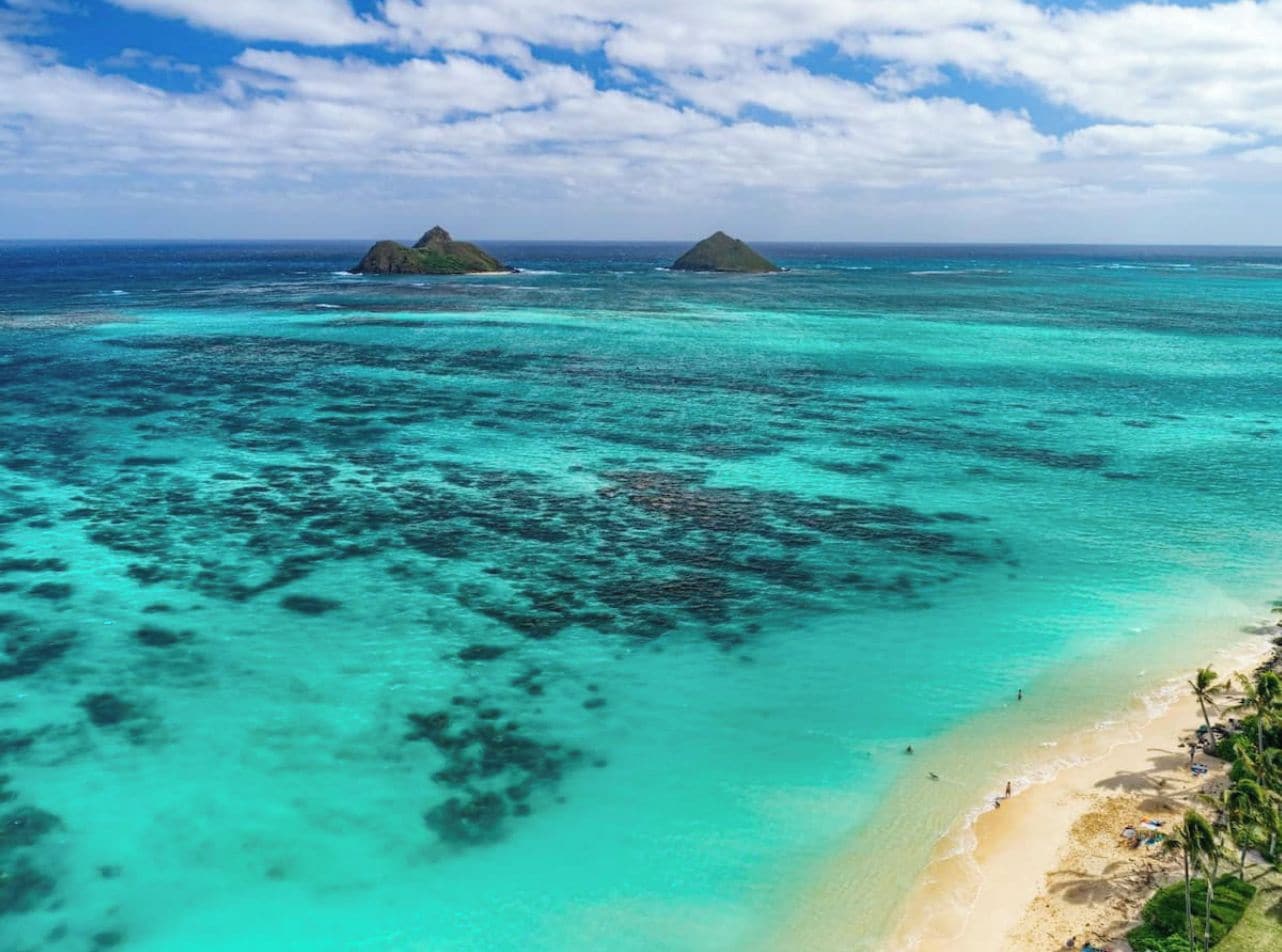 Una playa con aguas turquesas cristalinas, una orilla arenosa y dos islas pequeñas a lo lejos.