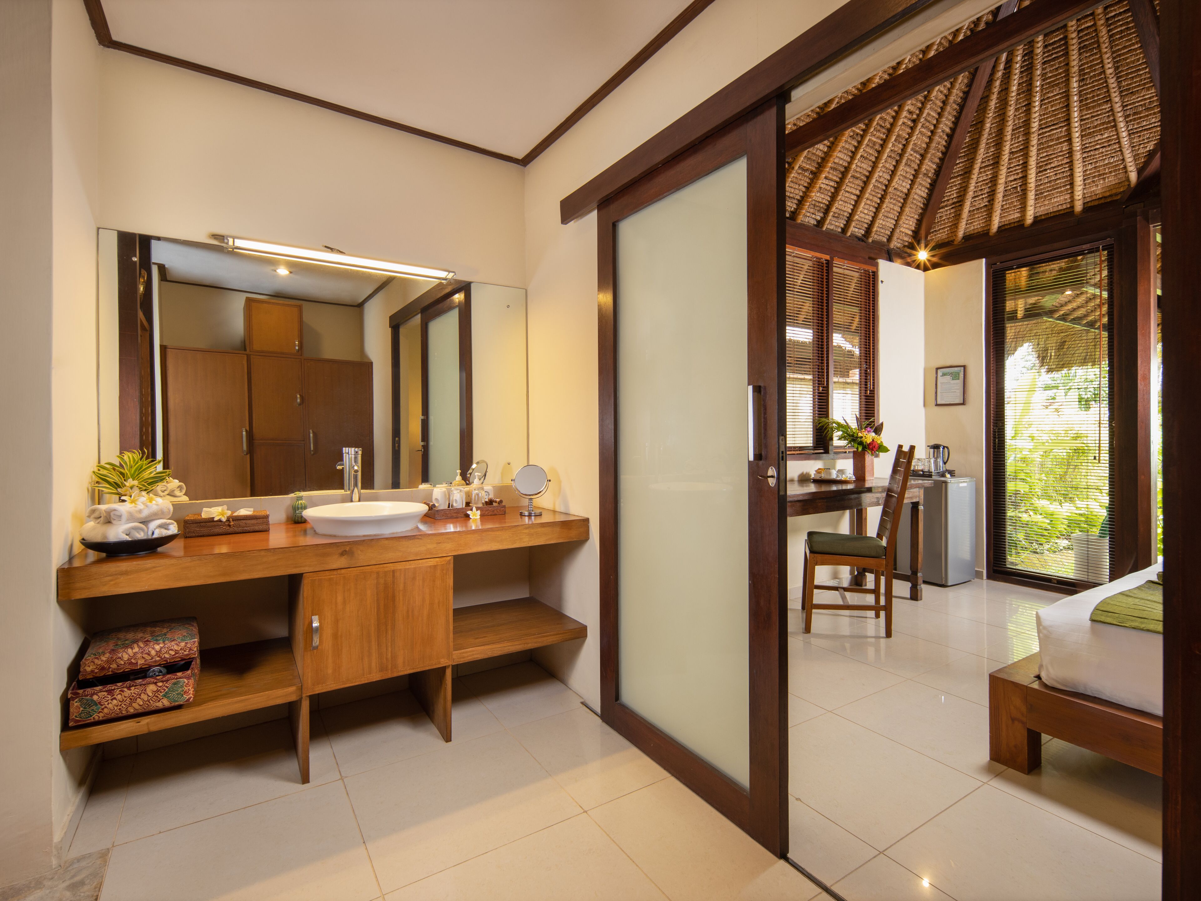 A modern bathroom with a large mirror, wooden vanity, and a sink. There is a chair and a small table with a plant and a vase.