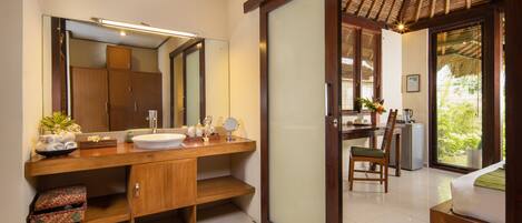 A modern bathroom with a large mirror, wooden vanity, and a sink. There is a chair and a small table with a plant and a vase.