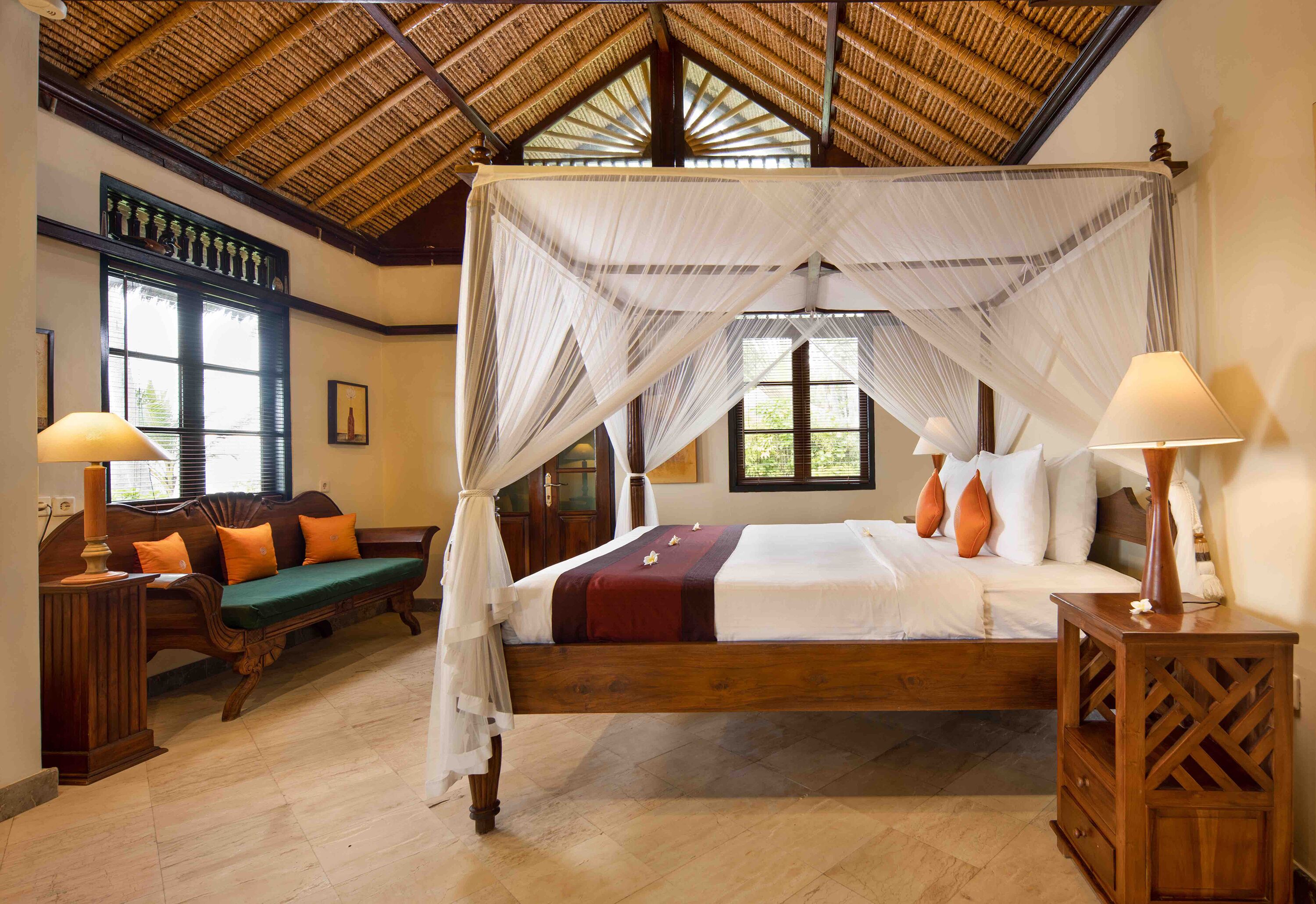 A four-poster bed with a canopy, a wooden bench, and a bedside table with a lamp.