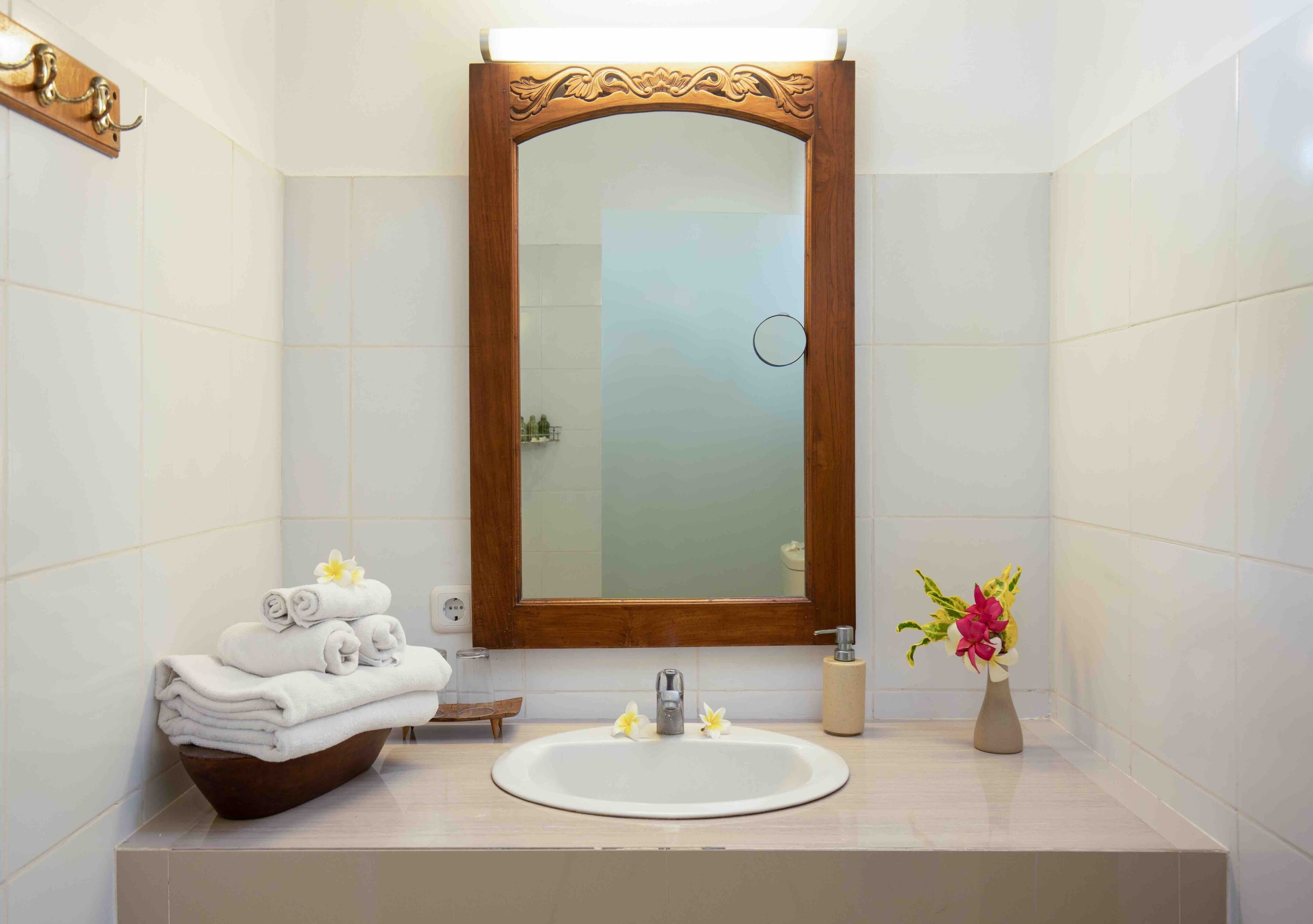 Un baño con un espejo de marco de madera, un lavabo blanco y una pila de toallas.