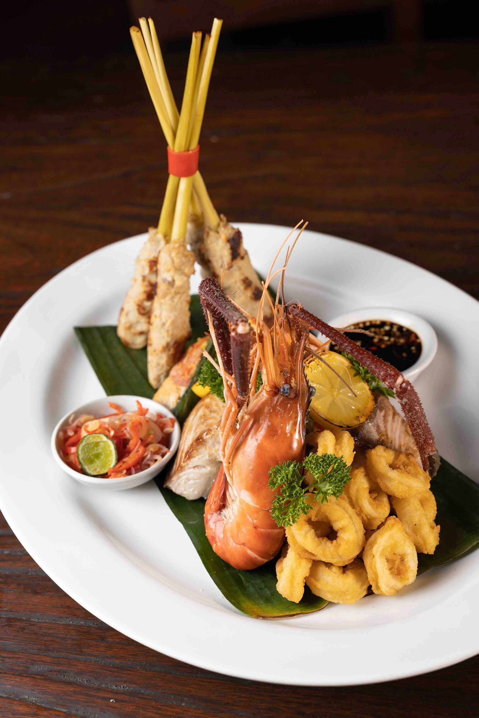 A plate of seafood including shrimp, squid rings, and grilled items, served with lemon and sauce.